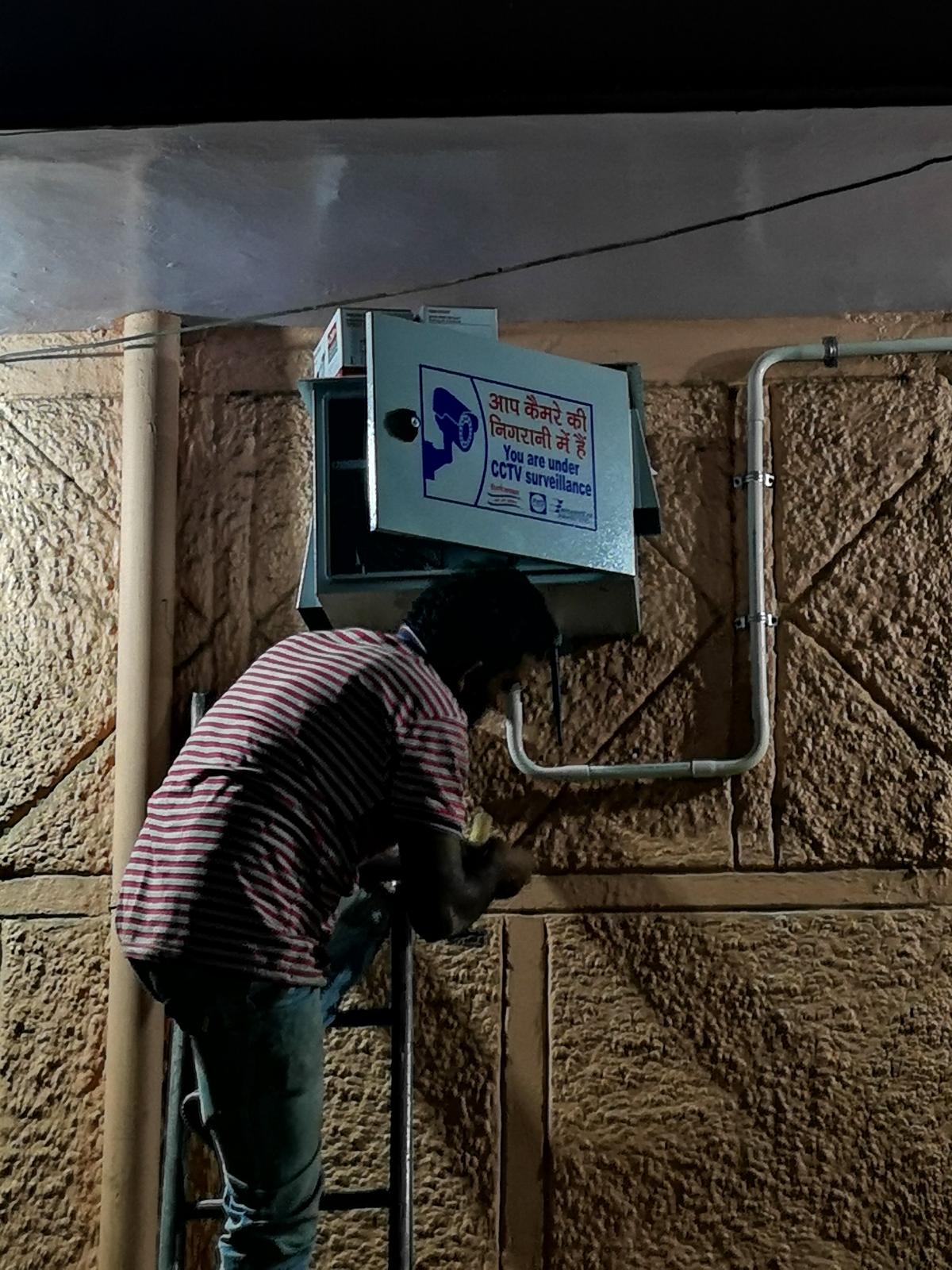 Technician working on a wall-mounted CCTV equipment enclosure with surveillance signage