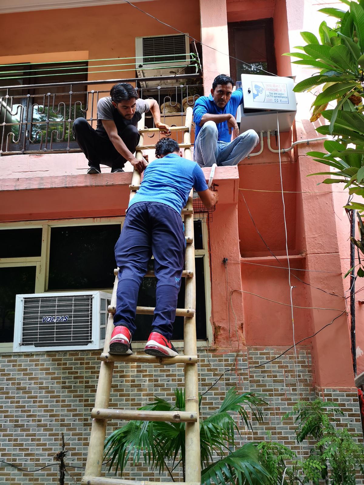 Installation team mounting a CCTV enclosure on a building facade using a ladder